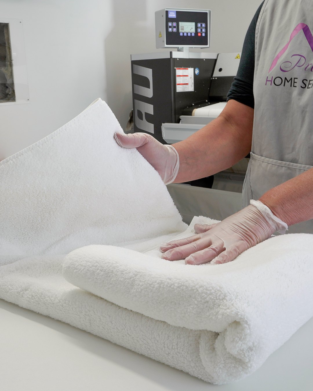 Mains gantées pliant une serviette blanche immaculée dans l'atelier Prestige Home Services